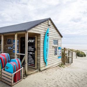 Une cabane en bois sur la plage, avec une pancarte indiquant les services proposés, tels que la location de planches de SUP, de kayaks et de matériel de planche à voile.