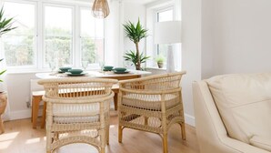 A bright, airy room with a dining table and chairs, large windows, and a sofa. - Mariners Stylish Beachside Getaway With Sea Views (Chichester)