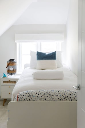 Une chambre à coucher avec un lit, une table de chevet blanche et une fenêtre avec des stores.