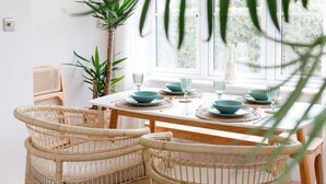 A dining area with a wooden table set for four, surrounded by wicker chairs, with a large window in the background. - Mariners Stylish Beachside Getaway With Sea Views (Chichester)