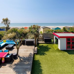 Une terrasse en bois avec des meubles d’extérieur, un petit abri de jardin et une vue sur la plage.
