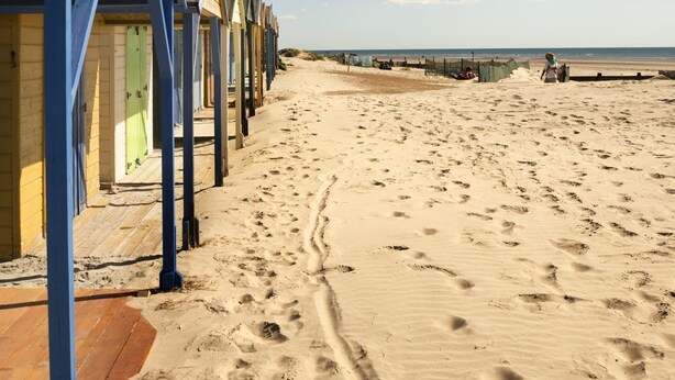 A row of beach huts with a sandy beach and the sea in the background. - Stylist Split Level 2 Bed With Parking (Chichester)
