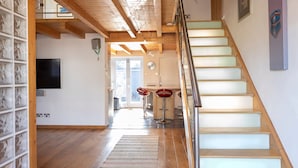 A spacious interior with a wooden staircase, a flat-screen TV, and a dining area with red bar stools. - Stylist Split Level 2 Bed With Parking (Chichester)