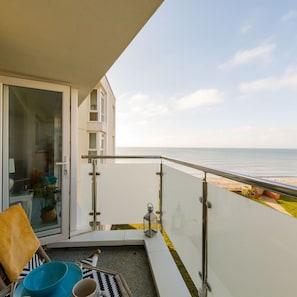 Ein Balkon mit Glastür, die zu einem Raum führt, ein Tischchen mit einem Stuhl und Blick auf den Strand.