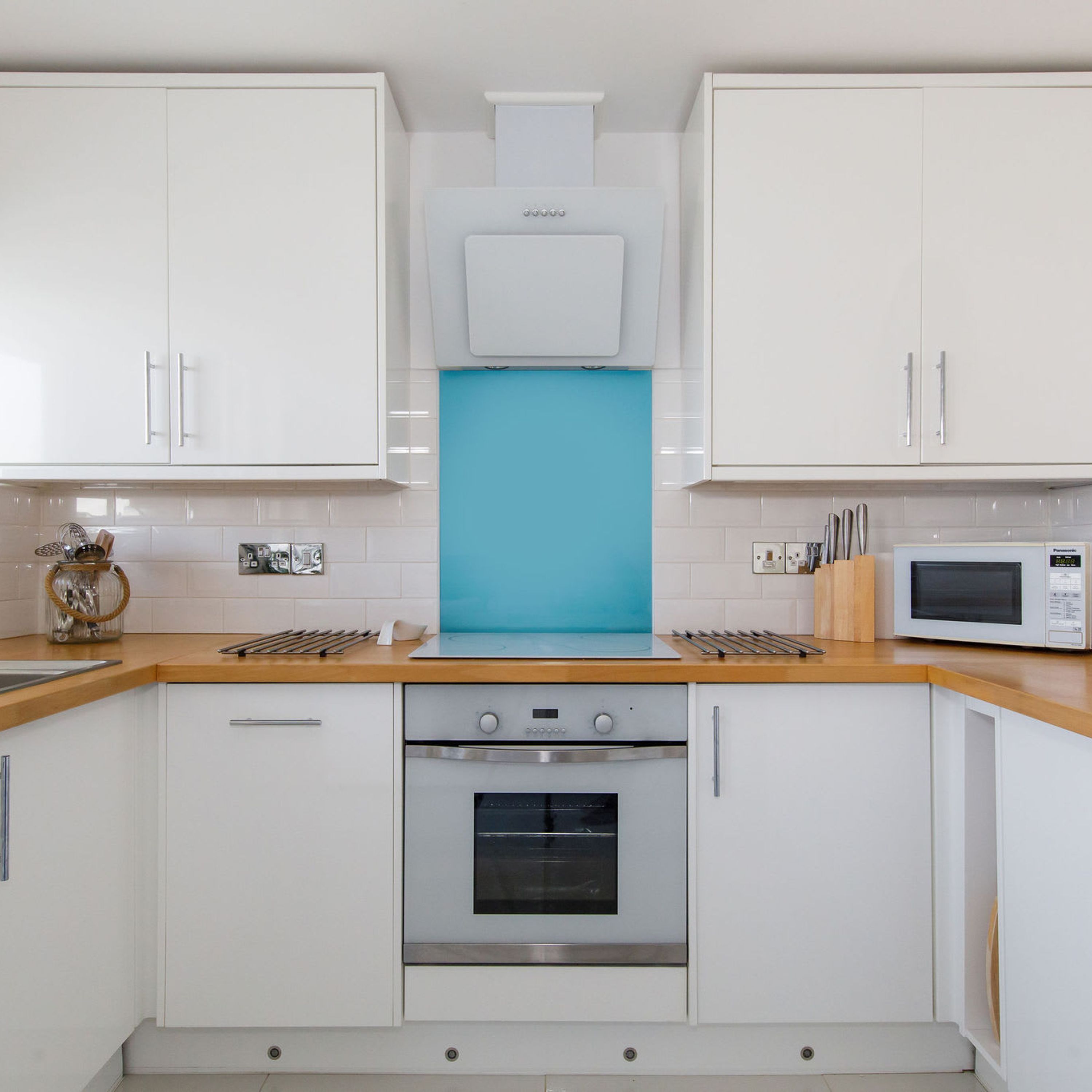 A modern kitchen with white cabinets, a blue backsplash, a built-in oven, and a microwave.