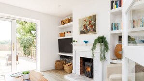A living room with a fireplace, bookshelves, a television, and a view of the outdoors. - 3bd Family Beach Retreat in West Wittering (Chichester)