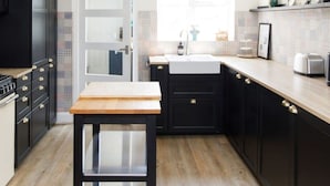 A modern kitchen with dark cabinets, a wooden countertop, and a small table. - 3bd Family Beach Retreat in West Wittering (Chichester)
