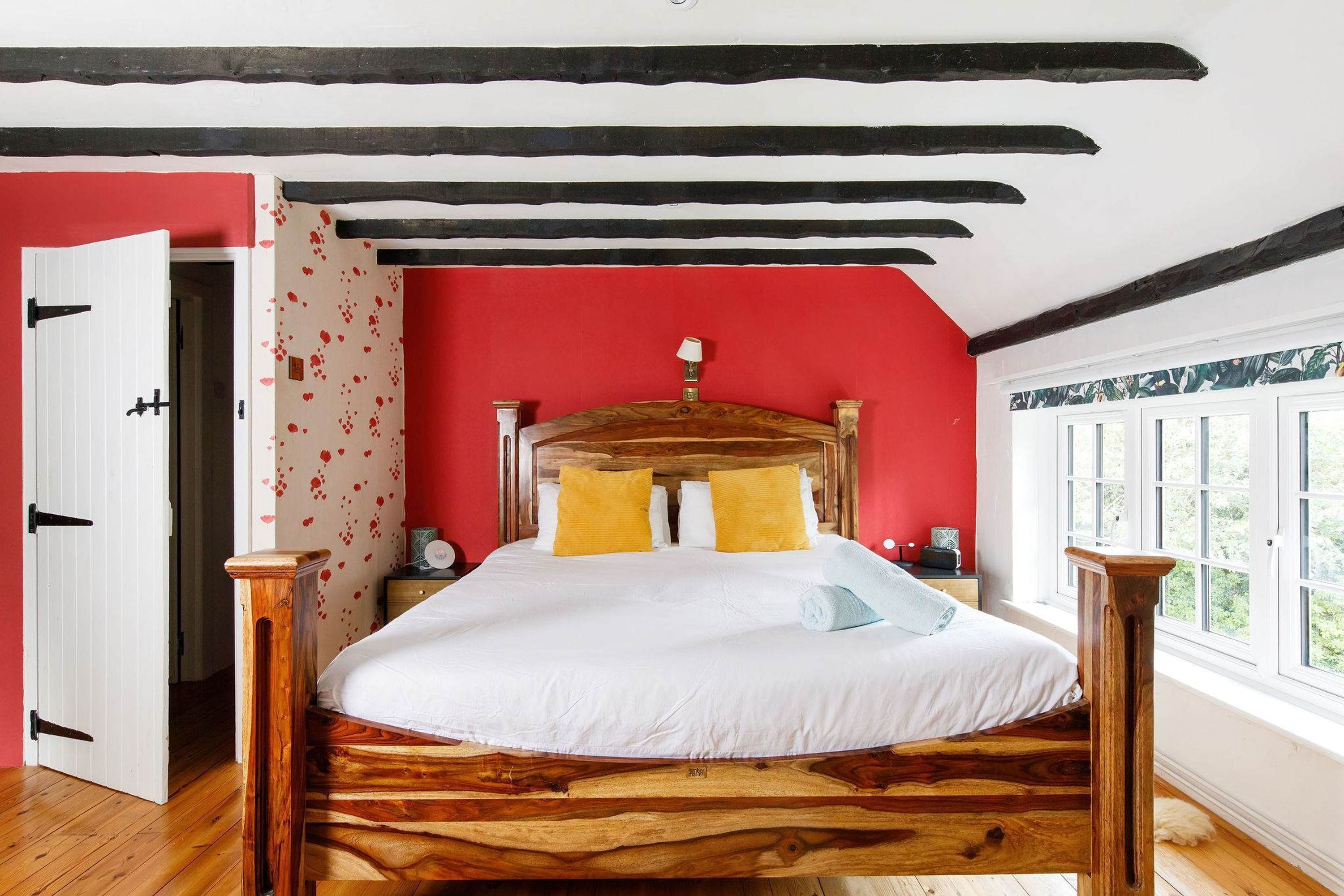 Ein hölzernes Bett mit weißer Matratze und gelben Kissen in einem Raum mit roten Wänden und einem großen Fenster.