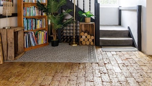 A staircase with a wooden railing, a bookshelf filled with books, a potted plant, and a yellow floor lamp. - Tranquil Luxe in Country Cottage (Chichester)