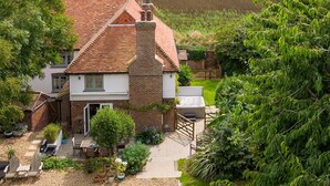A house with a brick chimney, a garden with potted plants, and a view of a field. - Tranquil Luxe in Country Cottage (Chichester)