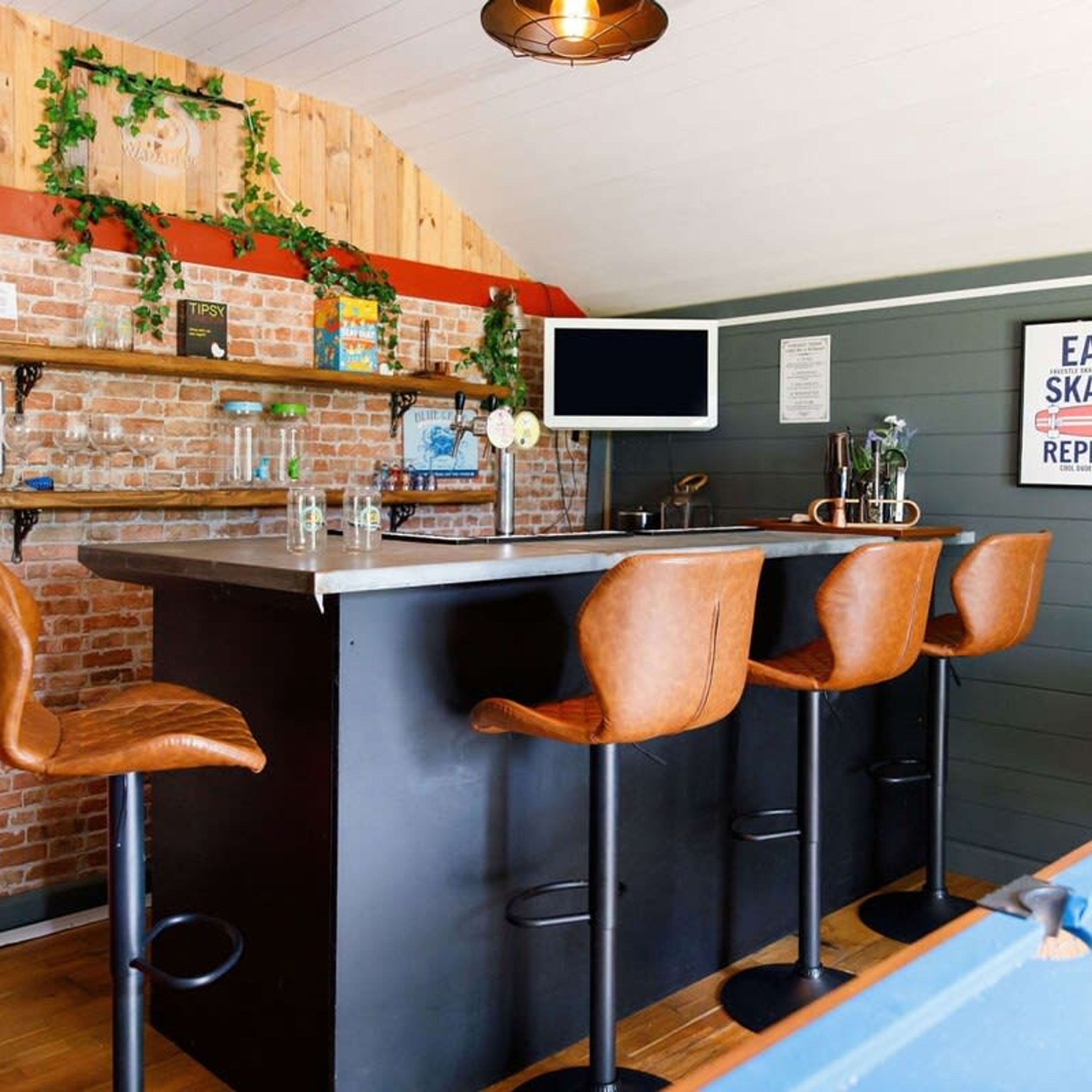 A bar area with a brick wall, wooden shelves, and leather bar stools.