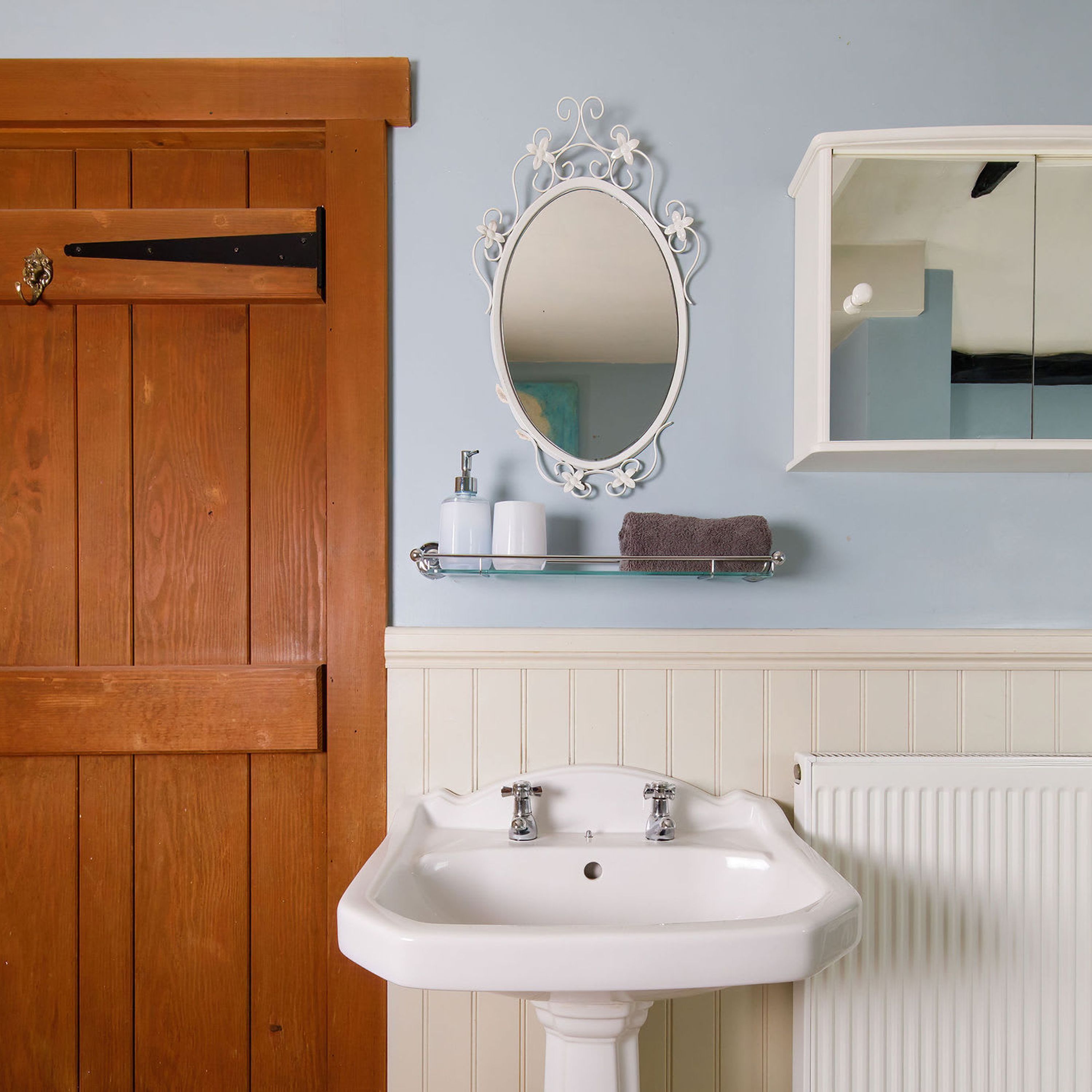 A bathroom with a wooden door, a white sink, a mirror, and toiletries on a shelf.