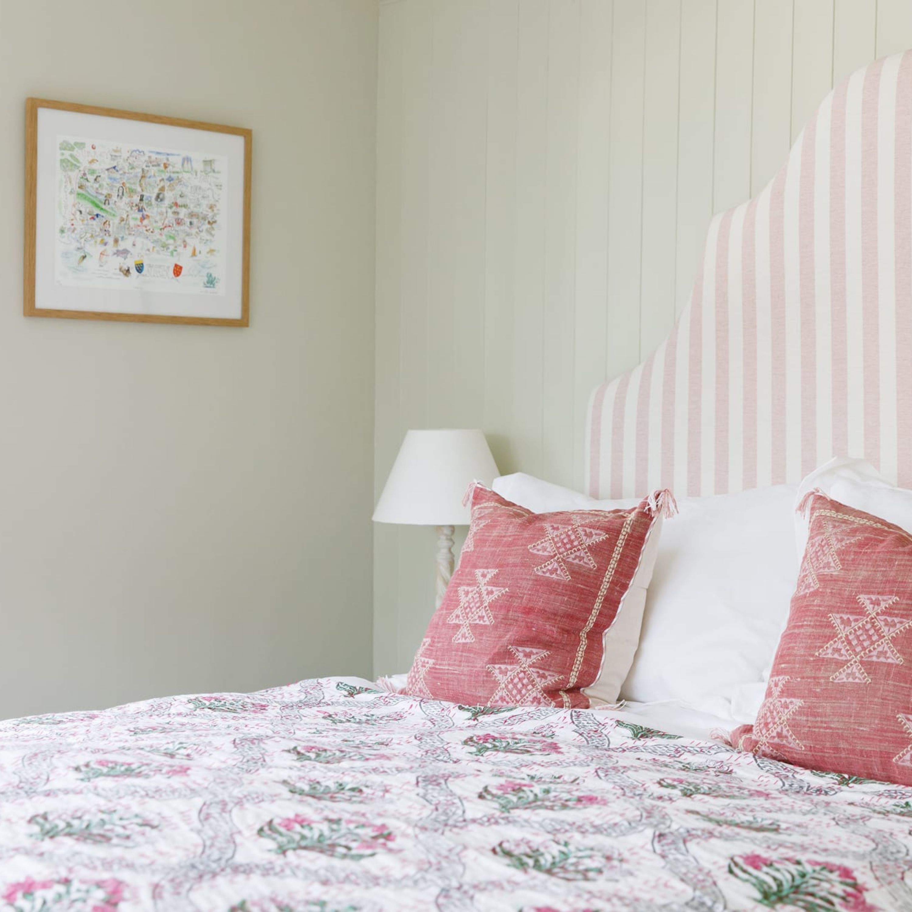 A bedroom with a bed, a lamp, and a framed map on the wall.