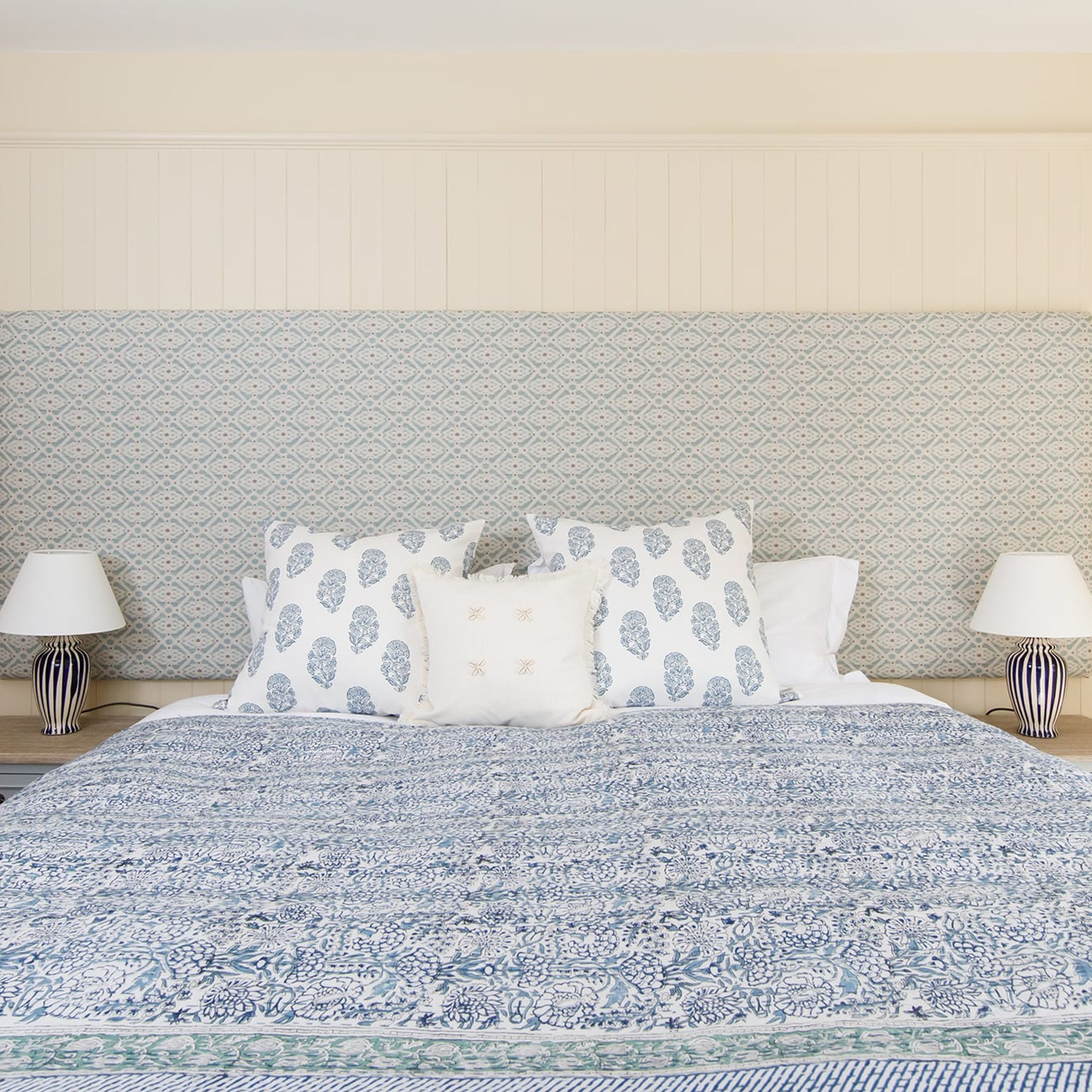 A bed with a patterned bedspread, two pillows with a leaf pattern, and two bedside lamps.