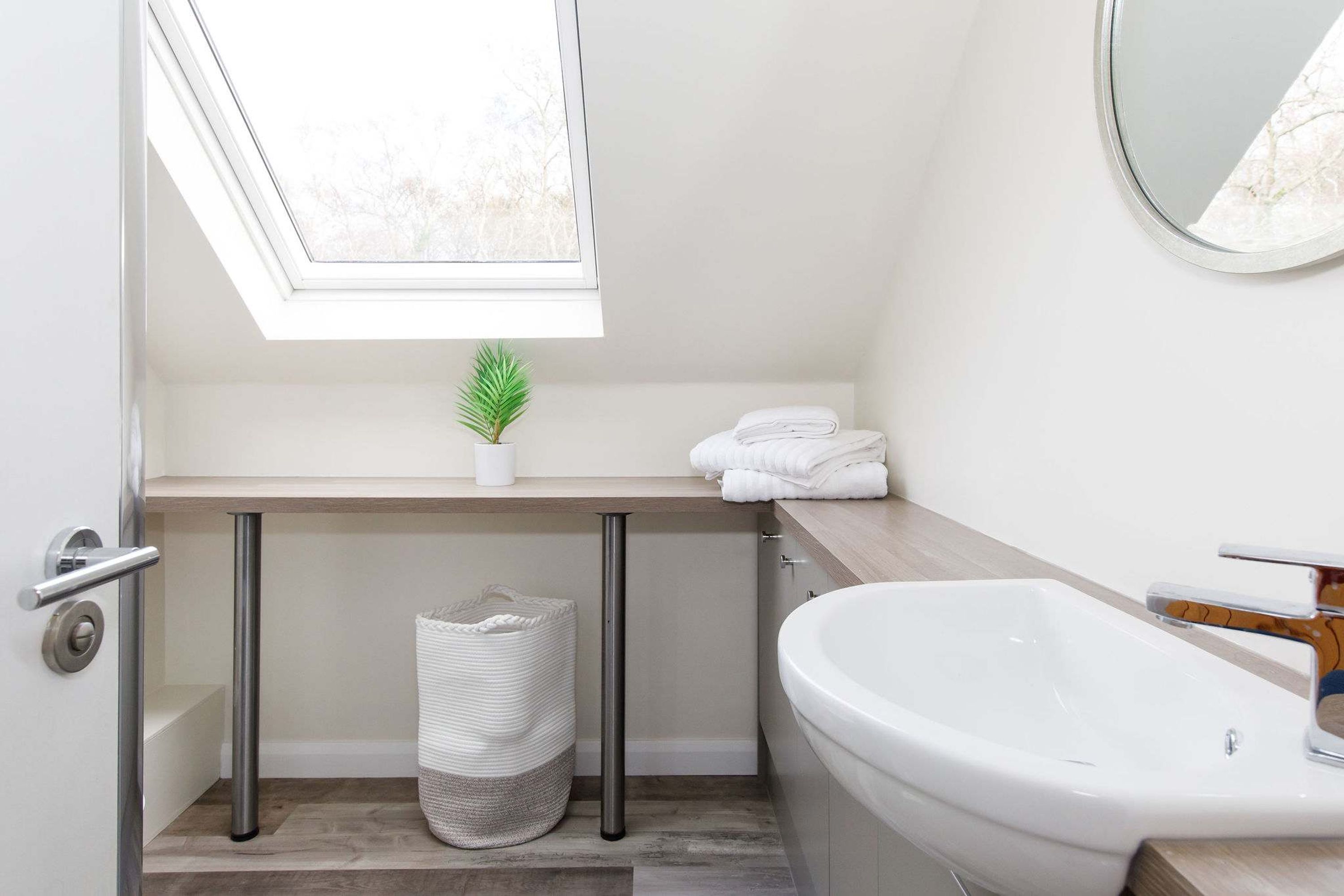 Un baño moderno con tragaluz, una bañera grande, un lavamanos y un perchero para toallas.