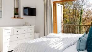 A bedroom with a bed, a dresser, a television, and a balcony with a view of trees. - Serene Riverside 6BR Luxury Retreat in Curdridge (Southampton)