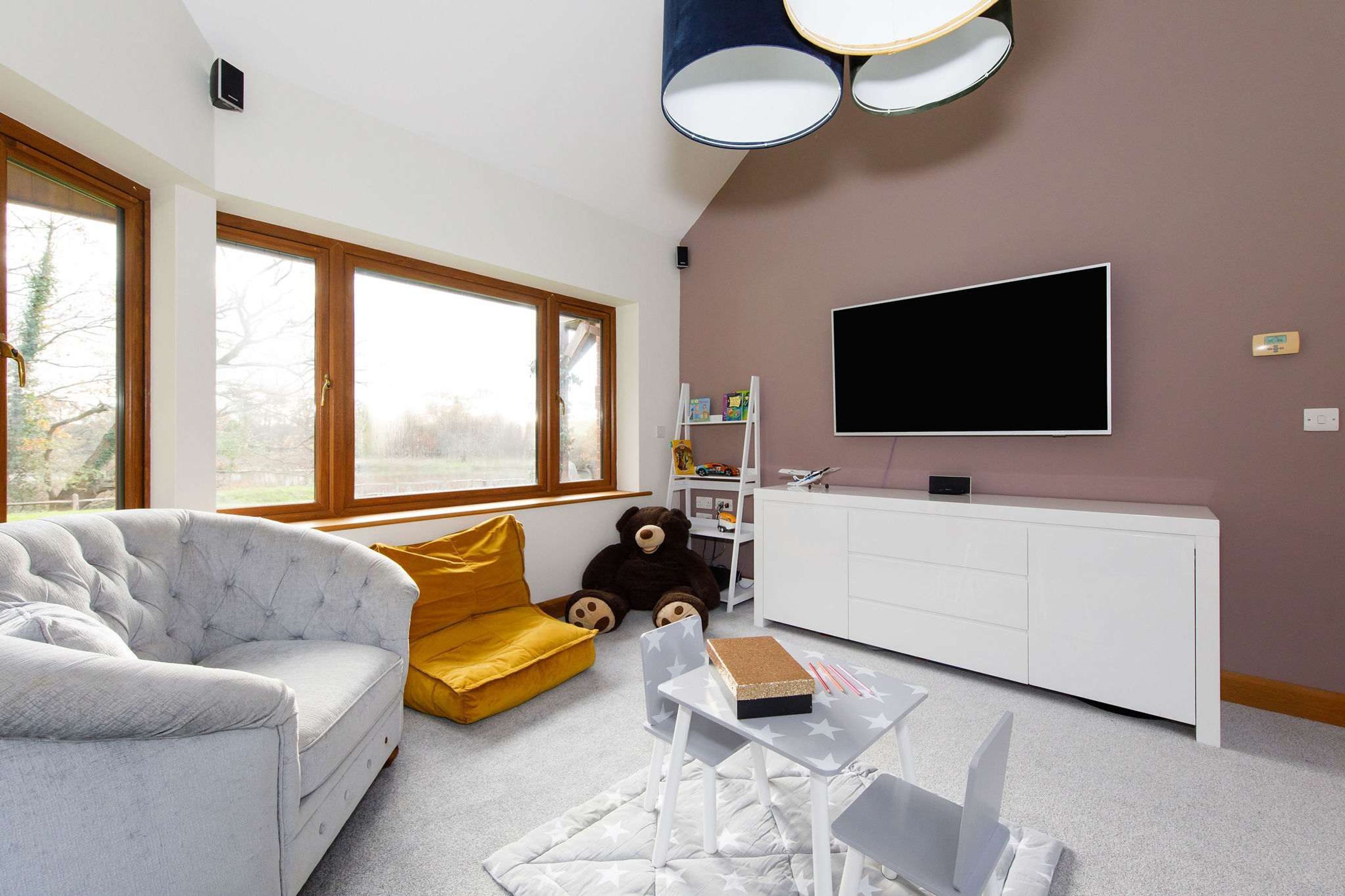 A modern living room with a sofa, a yellow accent chair, a white table with a book, a teddy bear, and a TV mounted on the wall.