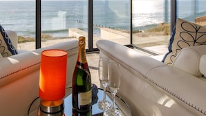 Ein Zimmer mit großem Fenster und Meerblick, eine Champagnerflasche und ein Glas auf einem Tisch.