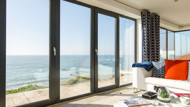 Ein modernes Wohnzimmer mit einem großen Glasfenster, das auf einen Balkon mit Meerblick führt.