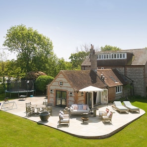 A brick house with a patio area featuring outdoor furniture, a trampoline, and a large pot. - Impressive Country Estate Sleeps 17 (Chichester)