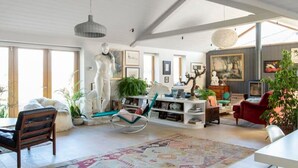 A spacious living room with a high ceiling, a large rug, a white sofa, a red armchair, and a dining area with a table and chairs. - Luxury Countryside Haven for 10 (Chichester)