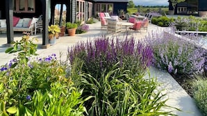 A covered outdoor seating area with multiple chairs and tables, surrounded by lush greenery and flowering plants. - Luxury Countryside Haven for 10 (Chichester)