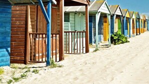 A row of beach huts with wooden exteriors and metal roofs, lined up along a sandy beach. - Luxury Countryside Haven for 10 (Chichester)