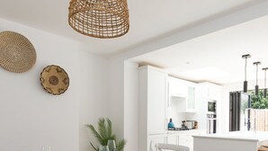 Un espace de repas moderne avec une table en bois dressée pour quatre personnes, des murs blancs et une vue sur la cuisine en arrière-plan.