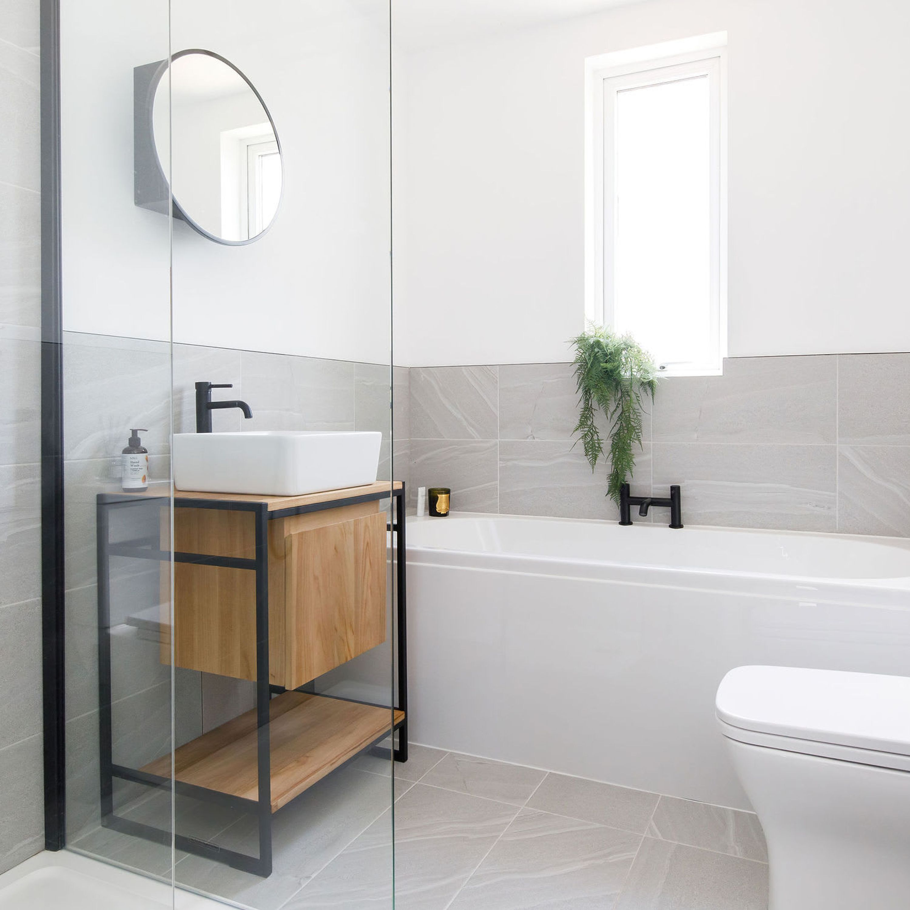 A modern bathroom with a glass-enclosed vanity, a freestanding bathtub, and a toilet.