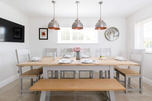 Un comedor con una mesa de madera dispuesta para seis personas, sillas blancas y tres lámparas colgantes.