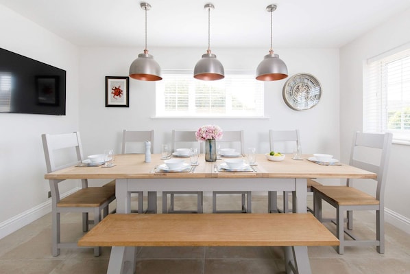 A dining area with a wooden table set for six, white chairs, and three pendant lights.