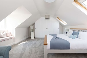 Un dormitorio con techo inclinado, cama con ropa de cama azul, mesita de noche, una silla y un armario.