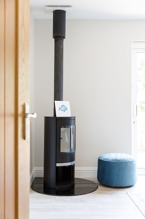 A modern wood-burning stove with a glass front, a blue ottoman, and a wooden door in the background.