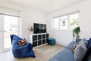 A modern living room with a blue bean bag, grey sofa, and a TV on a white cabinet.