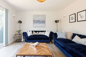 A modern living room with a dark blue sofa, a wooden coffee table, and a large painting on the wall.