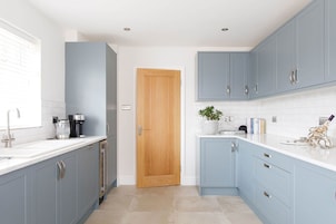 Una cocina moderna con armarios azul claro, encimeras blancas y una puerta de madera.