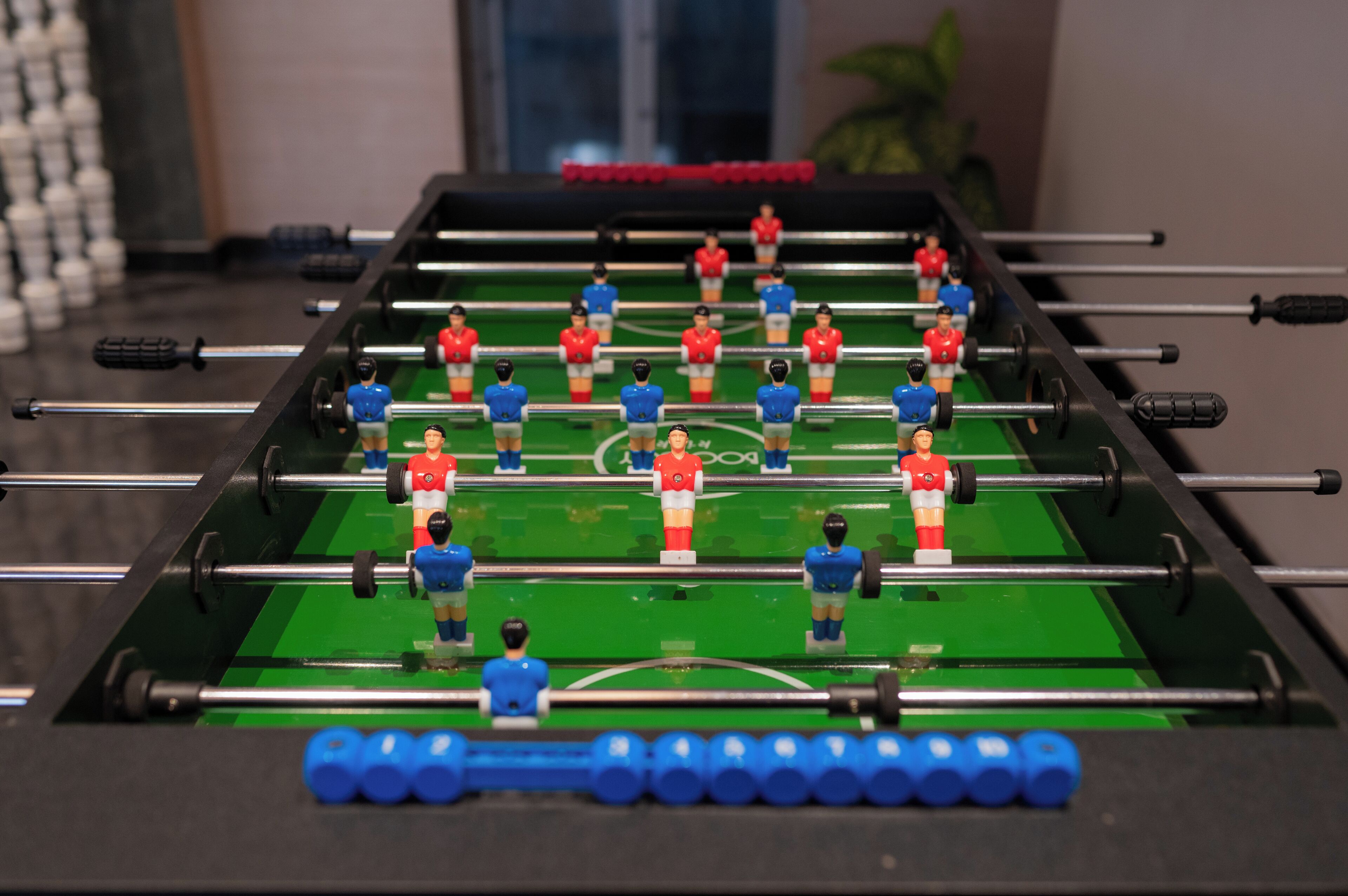 A foosball table with red and blue players, a green playing surface, and black rods.