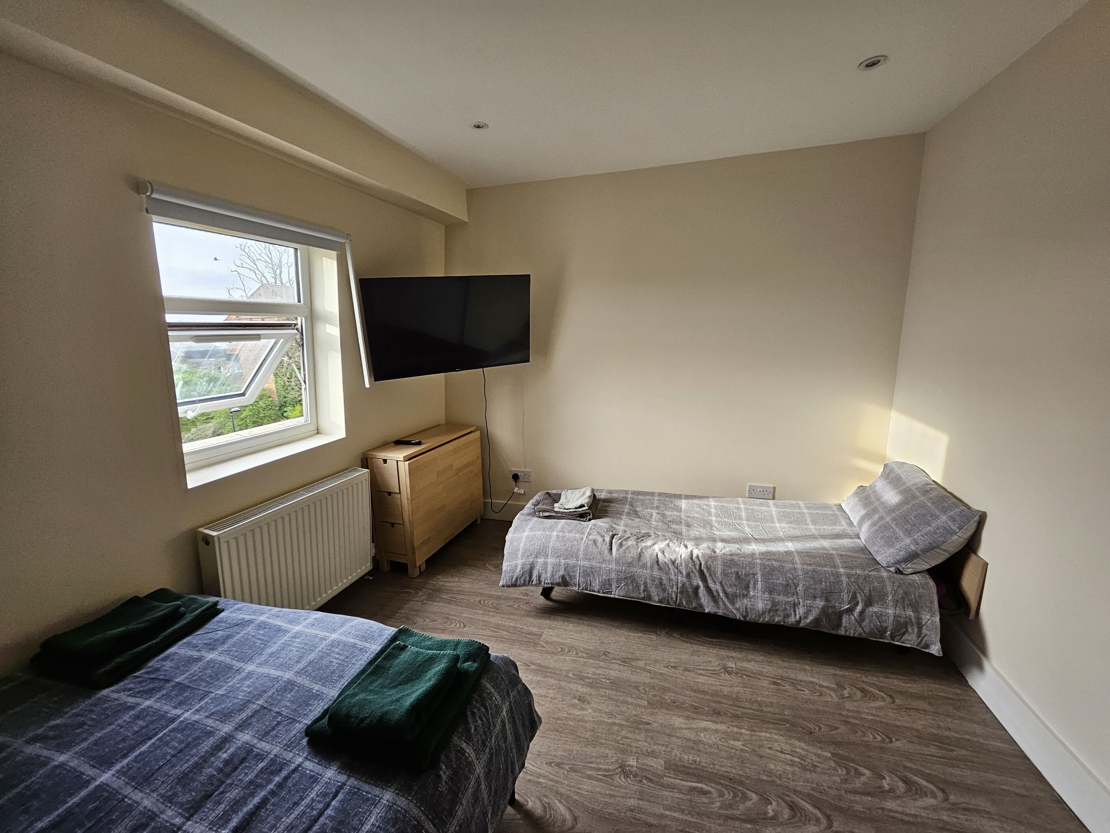 A bedroom with two beds, a TV, a window, and a radiator.