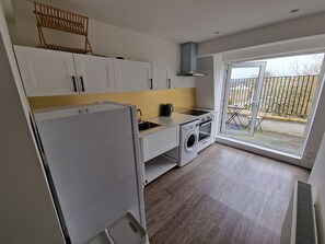 A compact kitchen with white cabinets, a built-in washing machine, and a window to the outside. - Impeccable 1-bed Apartment in London (London)