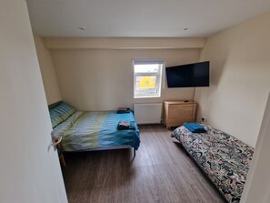 A small, well-lit room with two beds, a wooden dresser, a radiator, and a TV mounted on the wall. - Impeccable 1-bed Apartment in London (London)