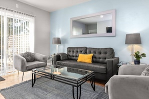 A modern living room with a grey sofa, a glass coffee table, and a grey armchair. There is a large mirror on the wall and a floor lamp. - A Fresh, Modern Home * Great Locale Near Downtown Appleton (Appleton)