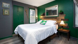 A bedroom with a green accent wall, a wooden headboard, a bedside table with a lamp, and a bed with white bedding. - Whimsical Magic Renovated Home - Walk to Downtown from Atlantic St. (Appleton)