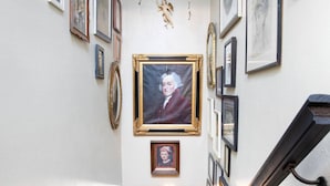 A hallway with framed portraits and a central painting on the wall. - Whimsical Magic Renovated Home - Walk to Downtown from Atlantic St. (Appleton)