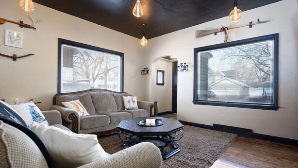 A living room with a sofa, armchairs, a coffee table, and large windows with blinds. - Whimsical Magic Renovated Home - Walk to Downtown from Atlantic St. (Appleton)
