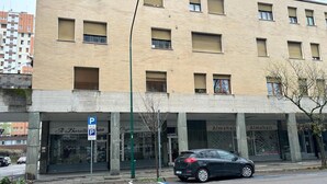 Un edificio con varias tiendas en la planta baja, incluyendo una cafetería y un salón de belleza. Se observa un cartel de estacionamiento que indica un área para vehículos.