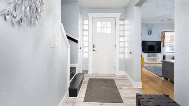 Un couloir menant à une porte blanche, un escalier, un salon avec un téléviseur et un canapé, et un élément décoratif mural.
