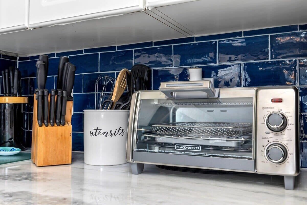 Une cuisine équipée d’un four grille-pain, d’un bloc à couteaux et d’une tasse sur laquelle est inscrit le mot « ustensiles ».