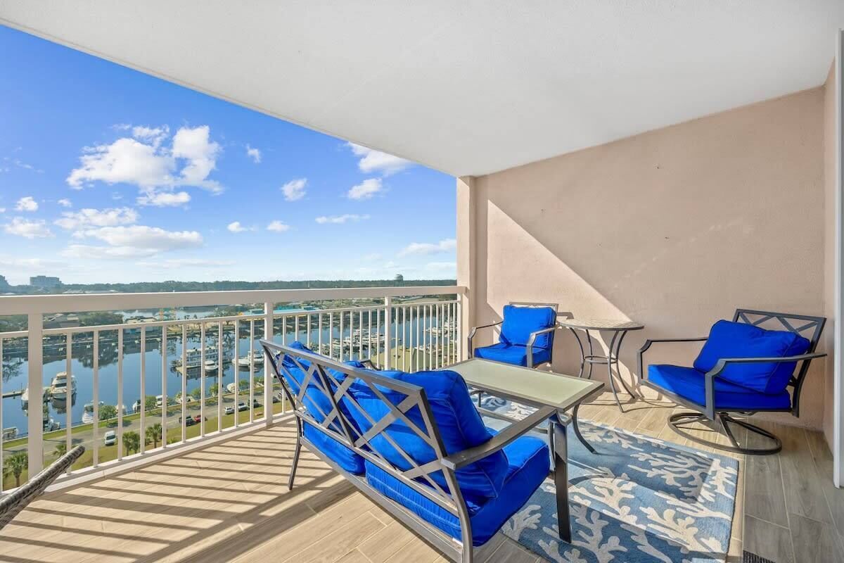 Een balkon met uitzicht op een jachthaven, een tafel met stoelen en blauwe kussens.