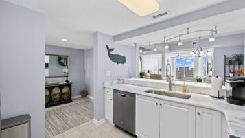 A modern kitchen with white cabinets, a dishwasher, a large island with a sink, and a whale decoration on the wall.