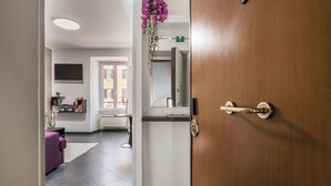 Un vestíbulo de hotel con mostrador de recepción, un sofá morado, una puerta de madera y un arreglo floral colgante.